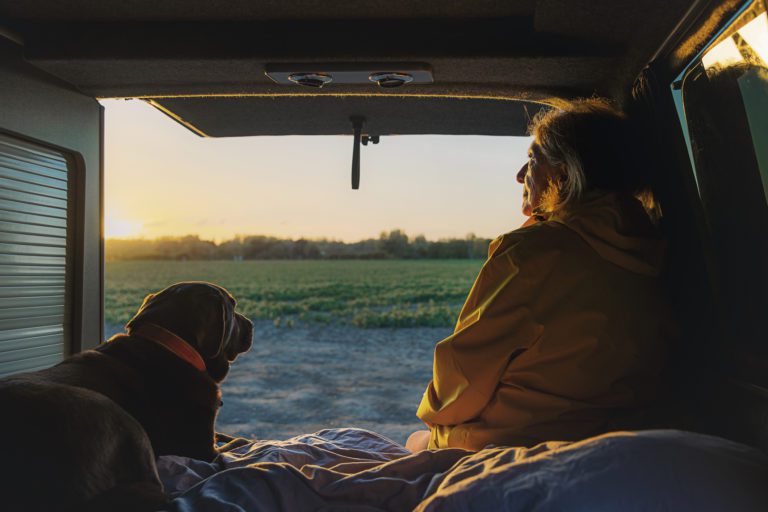 Senior woman and her pet dog looking at the view from the back of her campervan